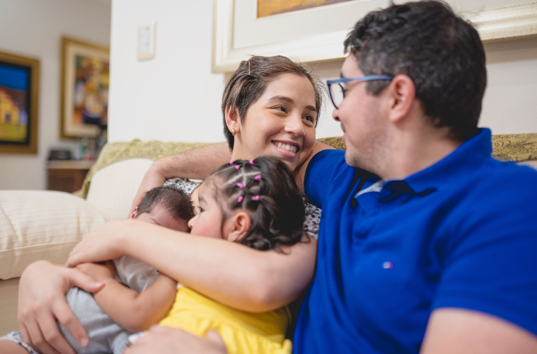 A man and woman hold two children in their arms and look towards each other. 