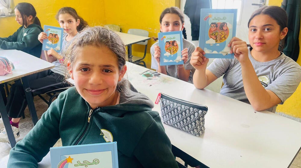 Young girls pose for a photo in a classroom with a book.