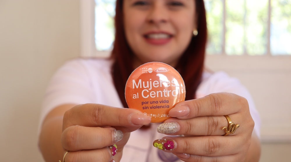 A woman holds a pin to the camera that states "Mujeres al centro"