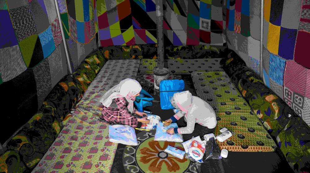 تجلس شابتان على الأرض وتنظران إلى محتويات مجموعات الكرامة الخاصة بهما - أكياس بها مستلزمات النظافة الأساسية.