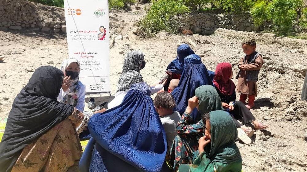 مجموعة من النساء والأطفال يجلسون ويتحدثون في الخارج على أرض صخرية