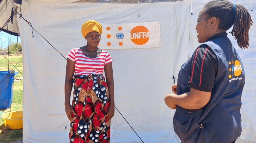  Une femme enceinte sourit à une femme vêtue d’un gilet de l’UNFPA, devant une tente